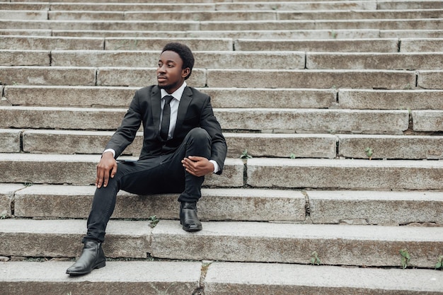 Young african american businessman wear black suit and sitting on stairs