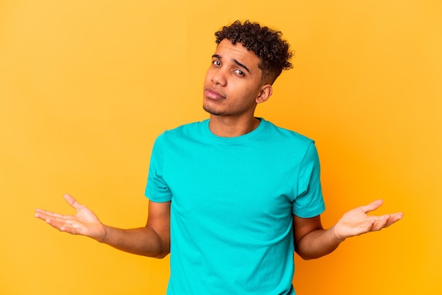 Young african american curly man isolated on purple doubting and shrugging shoulders in questioning gesture.