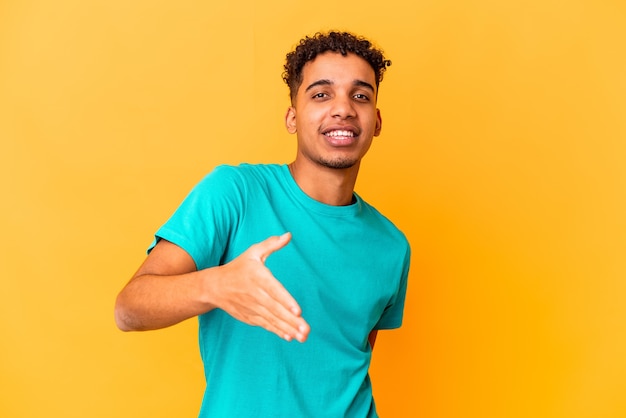 Young african american curly man on purple stretching hand at camera in greeting gesture.