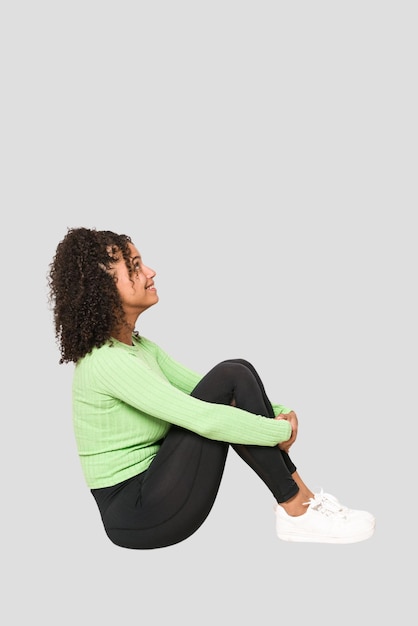 Young african american curly woman sitting on the floor isolated