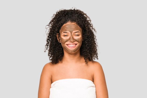 Young african american curly woman wearing a towel and a facial mask isolated