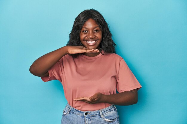 Young african american curvy woman holding something with both hands product presentation