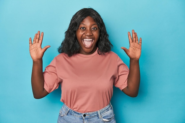 Young african american curvy woman receiving a pleasant surprise excited and raising hands