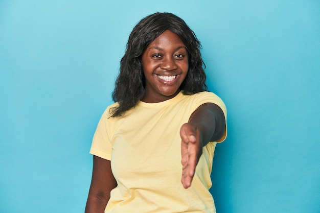 Young african american curvy woman stretching hand at camera in greeting gesture