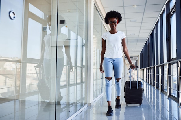 Young african american female passanger in casual clothes is in airport with baggage.