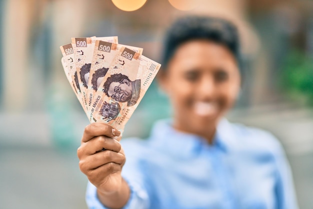 Young african american girl smiling happy holding one mexican 500 pesos banknote at the city