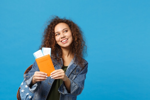 Young african american girl teen student in denim clothes, backpack hold pass isolated on blue wall