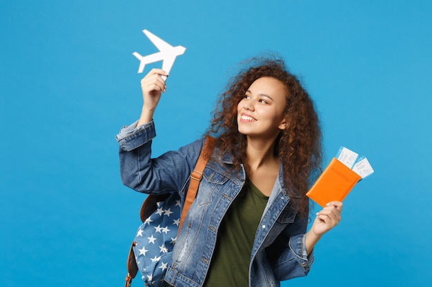 Young african american girl teen student in denim clothes, backpack hold pass isolated on blue wall