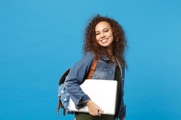 Young african american girl teen student in denim clothes, backpack hold pc isolated on blue wall