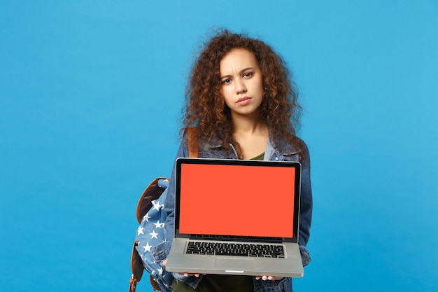 Young african american girl teen student in denim clothes, backpack work on pc isolated on blue wall