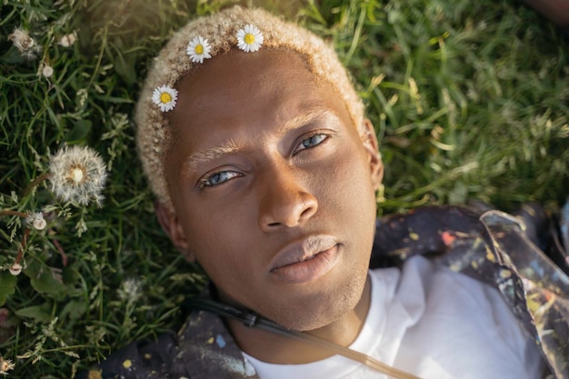 Young African American guy with stylish hair looking at camera laying on grass. Beauty concept