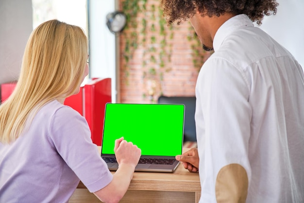 Young african american guy and young blonde girl in an office with laptop chroma green screen