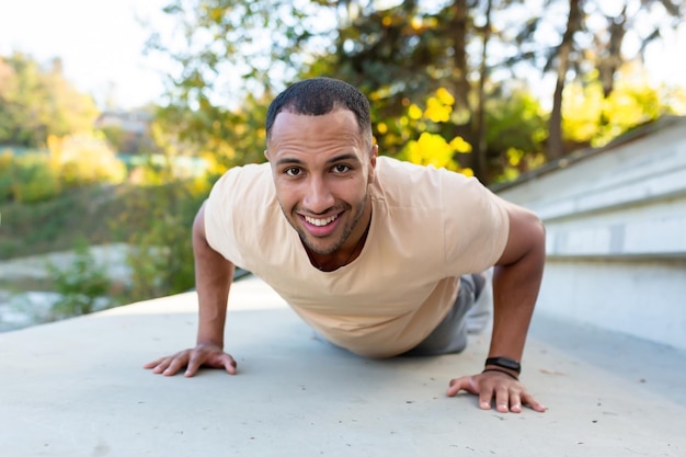 Young african american male athlete doing exercises in stadium on concrete stairs pushes up looks