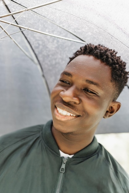 Young African American man under black umbrella in rain smiling Fall or spring weather