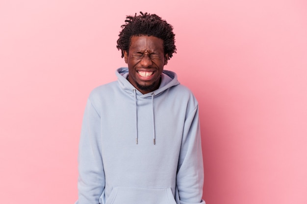 Young african american man isolated on pink background laughs and closes eyes, feels relaxed and happy.