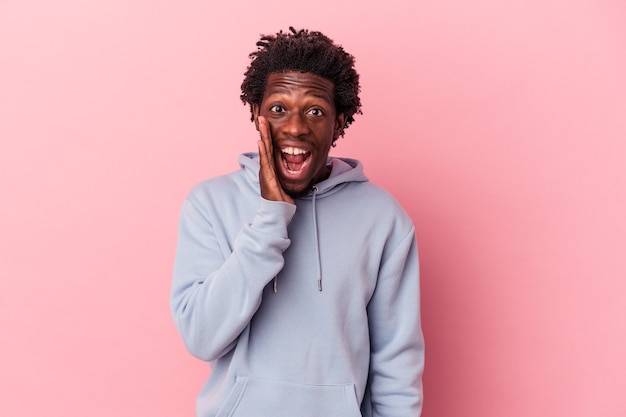 Young african american man isolated on pink background shouts loud, keeps eyes opened and hands tense.