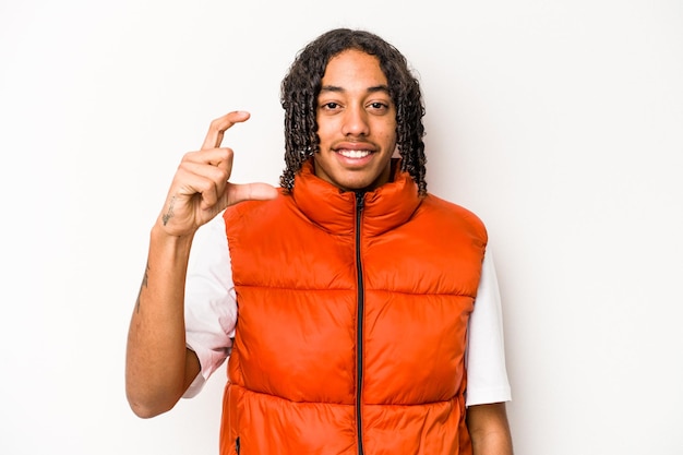 Young African American man isolated on white background holding something little with forefingers smiling and confident