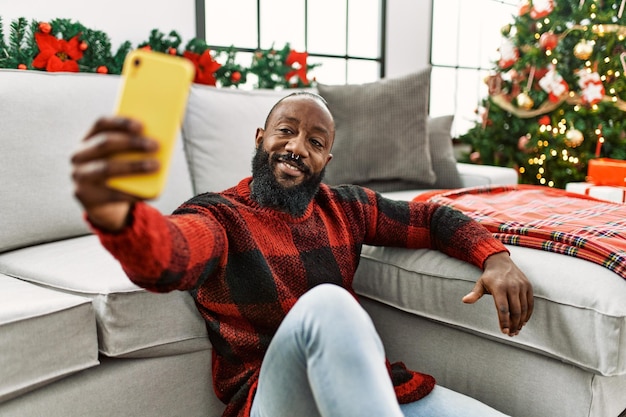 Young african american man make selfie by the smartphone sitting by christmas tree at home