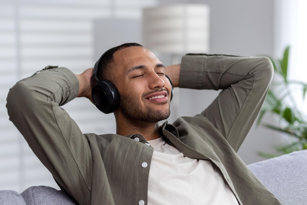 Young african american man relaxing at home wearing headphones listens to music podcast audiobook