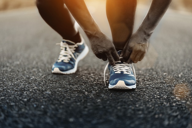 Young African American man runner tying shoelaces on road.