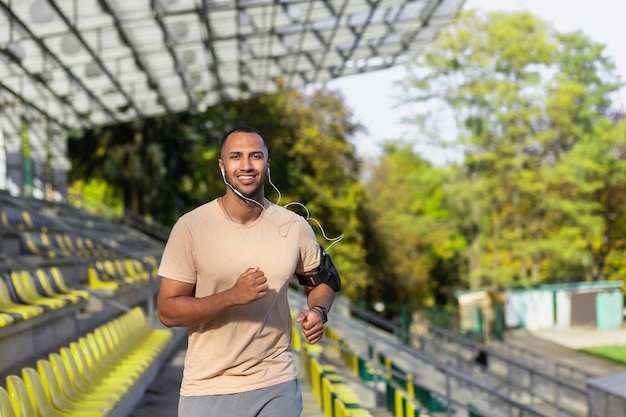 Young african american man sportsman track and field athlete running in headphones in the stadium