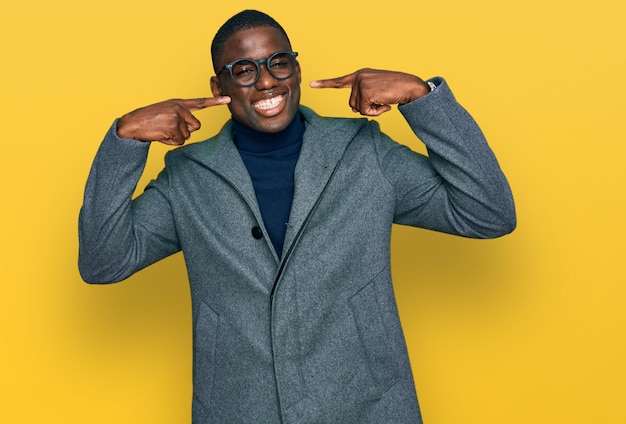 Young african american man wearing business clothes and glasses smiling cheerful showing and pointing with fingers teeth and mouth. dental health concept.