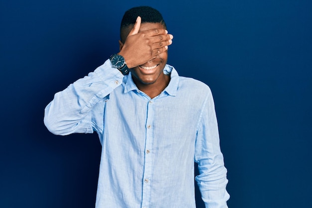 Young african american man wearing casual clothes smiling and laughing with hand on face covering eyes for surprise blind concept