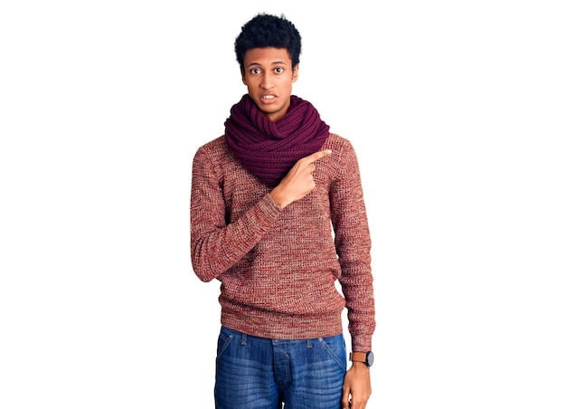 Young african american man wearing casual winter sweater and scarf pointing aside worried and nervous with forefinger, concerned and surprised expression