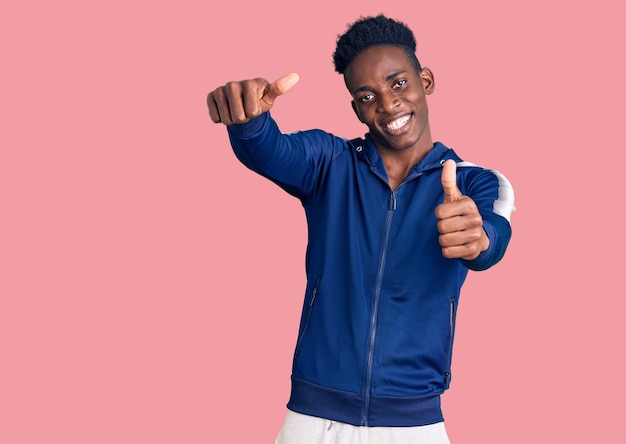 Young african american man wearing sportswear approving doing positive gesture with hand, thumbs up smiling and happy for success. winner gesture.