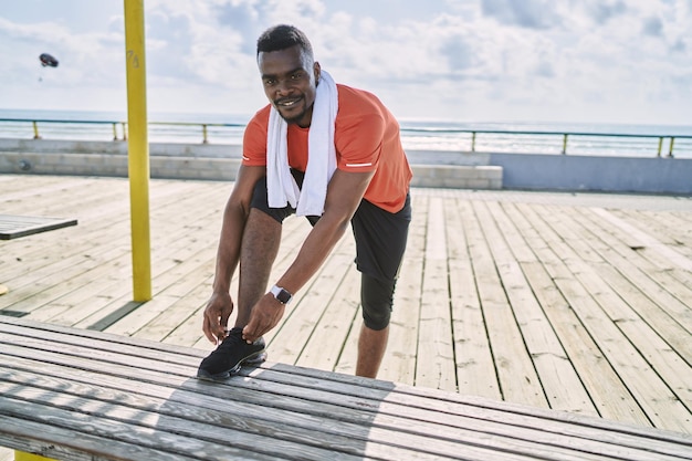 Young african american man wearing sportswear tying shoe at seaside