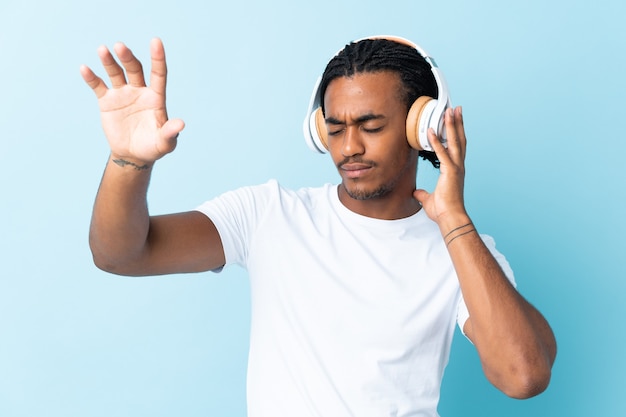 Young African American man with braids on blue listening music and dancing