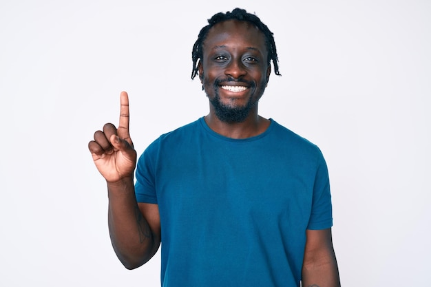 Young african american man with braids wearing casual clothes showing and pointing up with finger number one while smiling confident and happy.