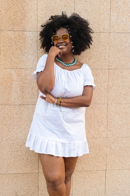 Young African American model with afro hairstyle with fashion glasses looking at the camera while standing on the street and smiling