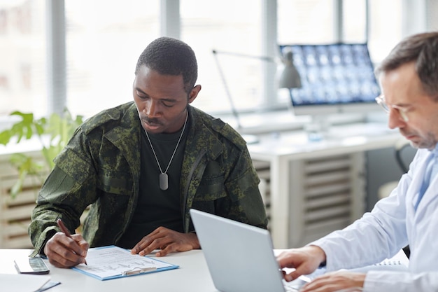 Young african american soldier having appointment in hospital making notes in medical questionnaire