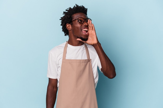 Young african american store clerk isolated on blue background shouting and holding palm near opened mouth.