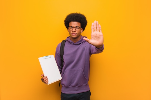 Young african american student man holding a clipboard putting hand in front