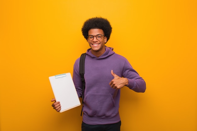 Young african american student man holding a clipboard smiling and raising thumb up