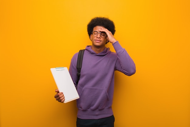 Young african american student man holding a clipboard worried and overwhelmed