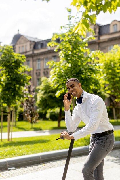 Young African American using mobile phone while standing with electric scooter on a street