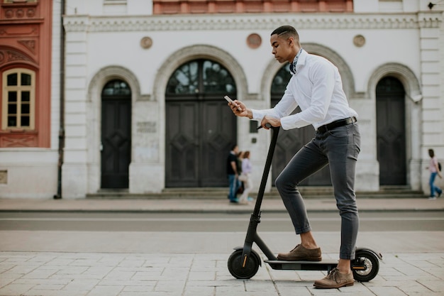 Young African American using mobile phone while standing with electric scooter on a street