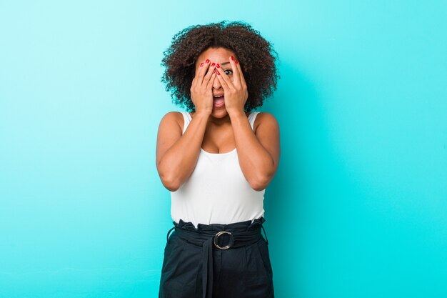 Young african american woman blink through fingers frightened and nervous.