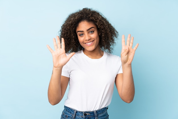 Young African American woman on blue wall counting nine with fingers