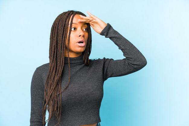 Young african american woman on blue wall looking far away keeping hand on forehead.