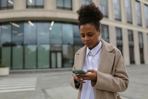 Young african american woman businessman typing on a mobile phone against the backdrop of a business