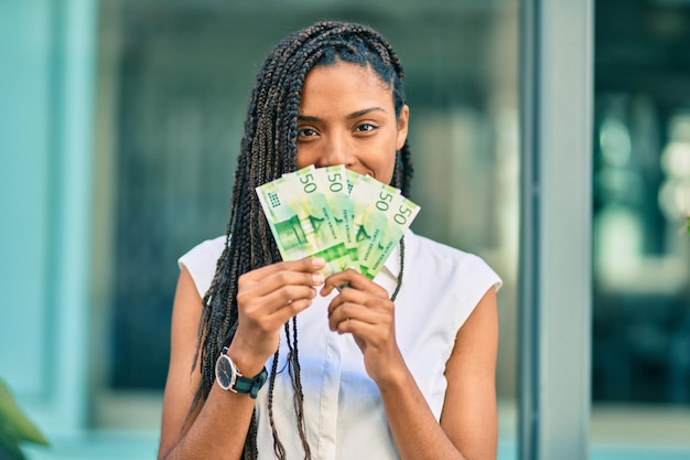 Young african american woman covering mouth with norwegian 50 krona banknotes at the city.