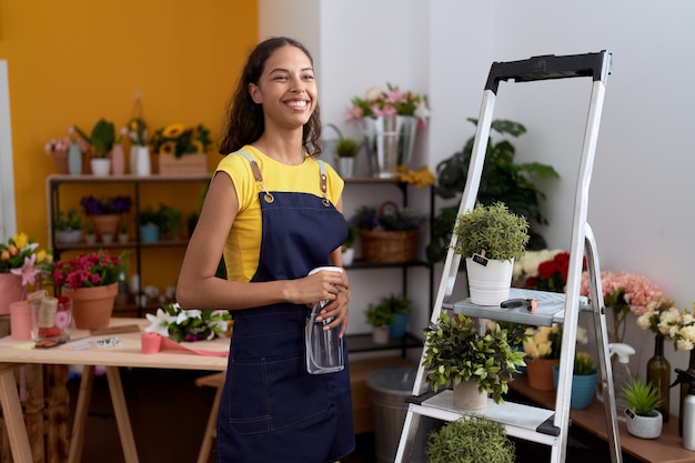 Young african american woman florist using diffuser watering plant at flower shop