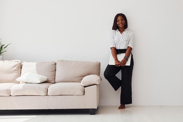 Young african american woman in formal clothes standing with laptop in hands indoors