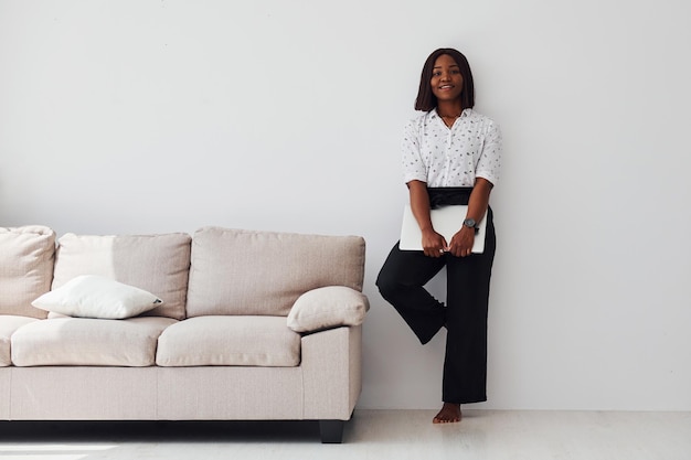 Young african american woman in formal clothes standing with laptop in hands indoors