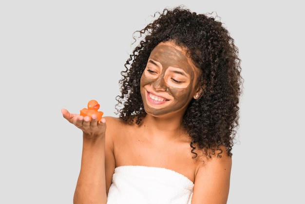 Young african american woman having a bath and a facial mask holding a rubber duck isolated