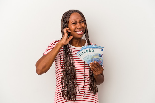 Young african american woman holding banknotes isolated on white background covering ears with hands.